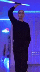 a woman in a black sweater and black pants is standing in a room with a blue light on the ceiling .