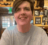 a woman is smiling in front of a wall with pictures and a green exit sign