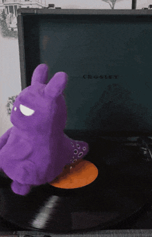 a purple stuffed animal is sitting on a record on a crosley turntable