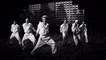a black and white photo of a group of people dancing in front of a building