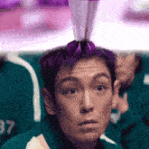 a man with purple hair is holding a purple object on top of his head .
