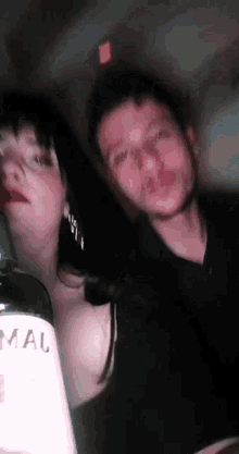 a man and a woman are posing for a picture with a bottle of alcohol in the foreground .