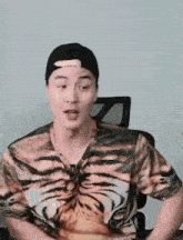 a man wearing a tiger print shirt and a hat is sitting in a chair .