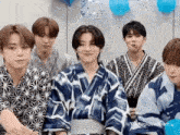 a group of young men wearing kimonos are sitting next to each other in a room .
