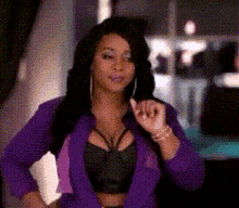 a woman in a purple jacket and black top is giving a thumbs up sign