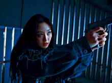 a woman in a blue jacket holds a gun in her right hand