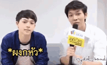 two young men are sitting next to each other on a couch with a microphone in front of them .