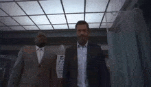 two men in suits are standing next to each other in a hallway .