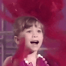 a little girl is standing in front of a red balloon and making a funny face .