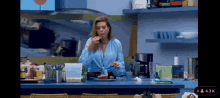 a woman in a blue shirt is sitting at a kitchen counter eating food