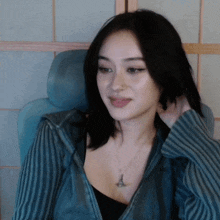 a woman wearing a striped jacket and a necklace is sitting in a chair and smiling