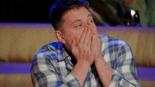 a man in a plaid shirt is covering his face with his hands