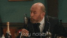 a man in a suit and tie stands in front of a microphone with the words " kissy noises " below him