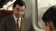 a man in a suit and tie is sitting on a train with another man .