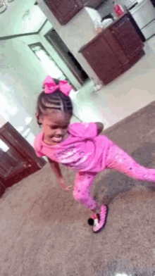 a little girl in a pink shirt and pink pants is dancing in a room .