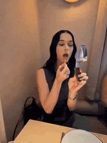 a woman is sitting at a table applying lipstick while looking in a mirror .