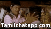 a man is hugging another man in a room with the words tamilchatapp com written on the bottom .