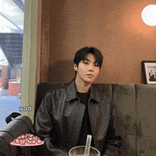a young man in a leather jacket sits on a couch with a cup of coffee and a sticker that says yad