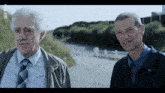 two men are standing next to each other on a road and one of them has a missing tooth