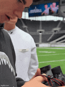 a man in a shark shirt is holding a camera in front of a screen that says imgflip.com