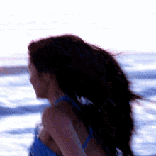 a woman in a blue top is standing in front of a body of water