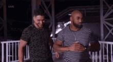 two men are standing next to each other on a bridge at night .