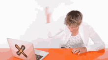 a woman is sitting at a desk with a pink laptop with a cross on it