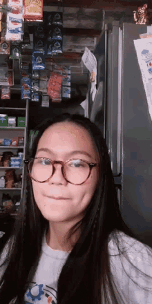 a girl wearing glasses is standing in front of a refrigerator in a store