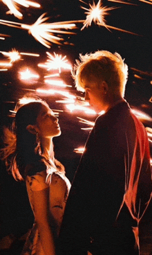 a man and a woman are looking at each other in front of sparklers