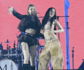 two women are dancing on a stage with a drum set in the background .
