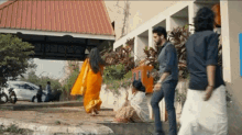 a group of people are standing outside of a building including a woman in an orange sari