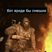 a man in a hood is standing in front of a fire with a caption in a foreign language .