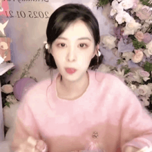 a woman wearing a pink sweater is sticking her tongue out in front of flowers