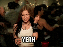 a woman in a white tank top says yeah in a crowded room