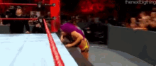 a female wrestler is standing on the edge of a ring .