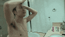 a shirtless man adjusts his hair in front of a mirror