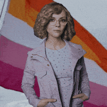 a woman wearing glasses and a purple jacket stands in front of a lesbian flag