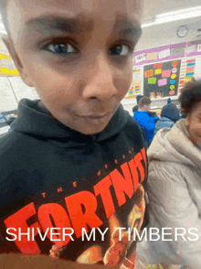 a young boy wearing a fortnite hoodie is standing in a classroom