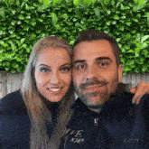 a man and a woman are posing for a picture and the man is wearing a sweatshirt that says " i love john "