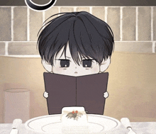 a boy is reading a book while sitting at a table with a plate of food