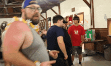 a group of men are standing in a room with one wearing a red shirt