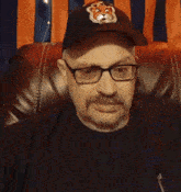 a man wearing glasses and a baseball cap is sitting on a leather chair
