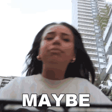 a woman in a white shirt says maybe in front of a building