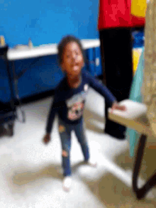 a little girl in a blue shirt is laying on her back on the floor .
