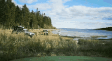 a man in a white shirt stands on a grassy beach near a lake