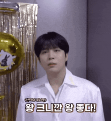 a man in a white shirt is standing in front of a gold curtain and balloons