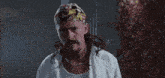 a man wearing a bandana and a necklace is standing in front of a sign that says ding