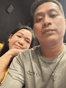 a man and a woman are posing for a picture and the man has a cross necklace