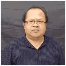 a man wearing glasses and a blue striped shirt is making a face .
