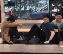 three men are sitting on a conveyor belt with a sign that says impacte